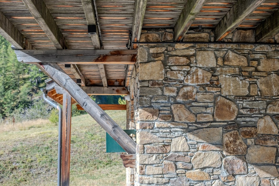 Mur en pierres apparentes et charpente en bois d'un chalet de montagne, en lumière rasante