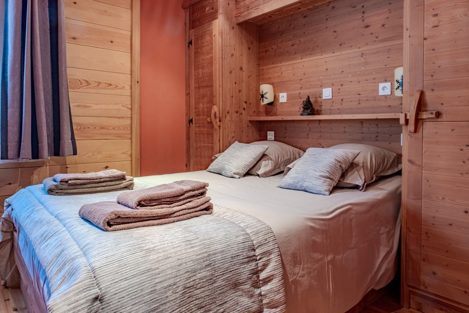 Lit en bois avec oreillers, couverture rayée et serviettes pliées dans une chambre du chalet