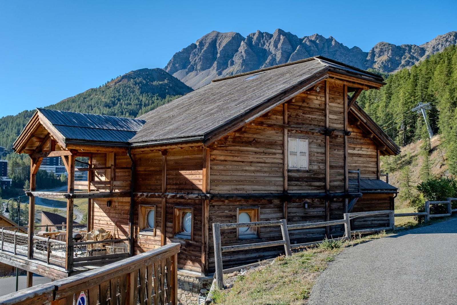 Façade en bois du chalet et sa terrasse couverte, au pied des sommets rocheux de Vars